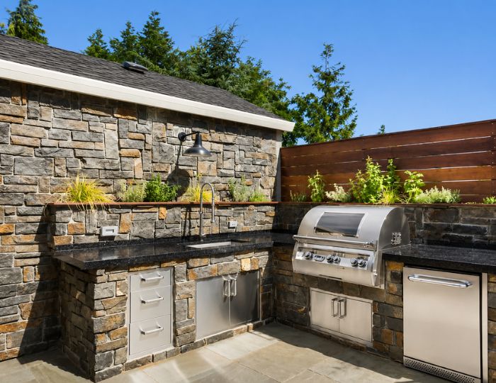 Outdoor kitchen with protected natural stone countertops under pergola shade